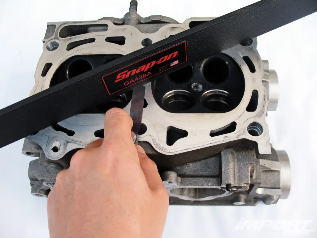 Professional mechanic using straight edge and feeler gauge to precisely check engine block flatness before automobile engine gasket installation.