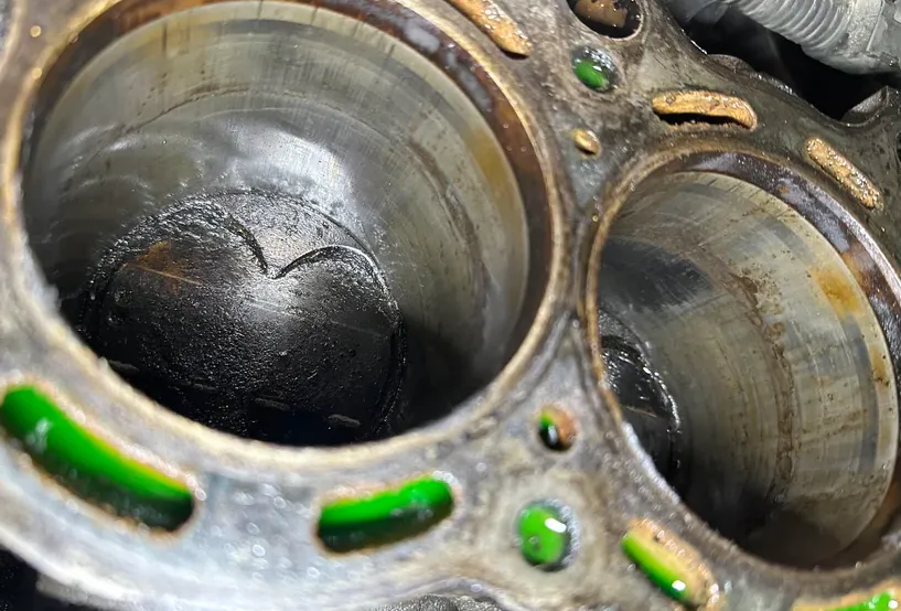 Close-up shot of a removed cylinder head showing gasket failure, carbon tracking between cylinders, and coolant leakage.