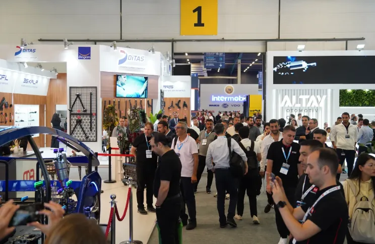An inside view of a crowded exhibition hall, focusing on modern automotive parts displays, brightly lit booths, and professionals engaged in deep business discussions