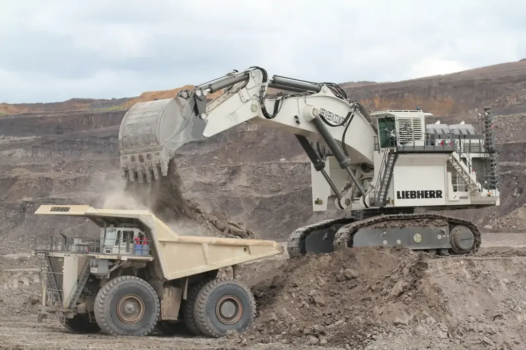 Massive Liebherr R9800 mining excavator loading a 360-ton haul truck in an open-pit mine during sunrise, showing the machine’s enormous bucket and hydraulic system.